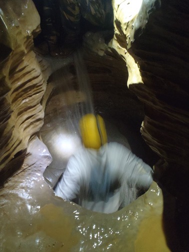 One of our group pulling himself up through a hole in a chamber ceiling into the chamber with the 396-ft waterfall.